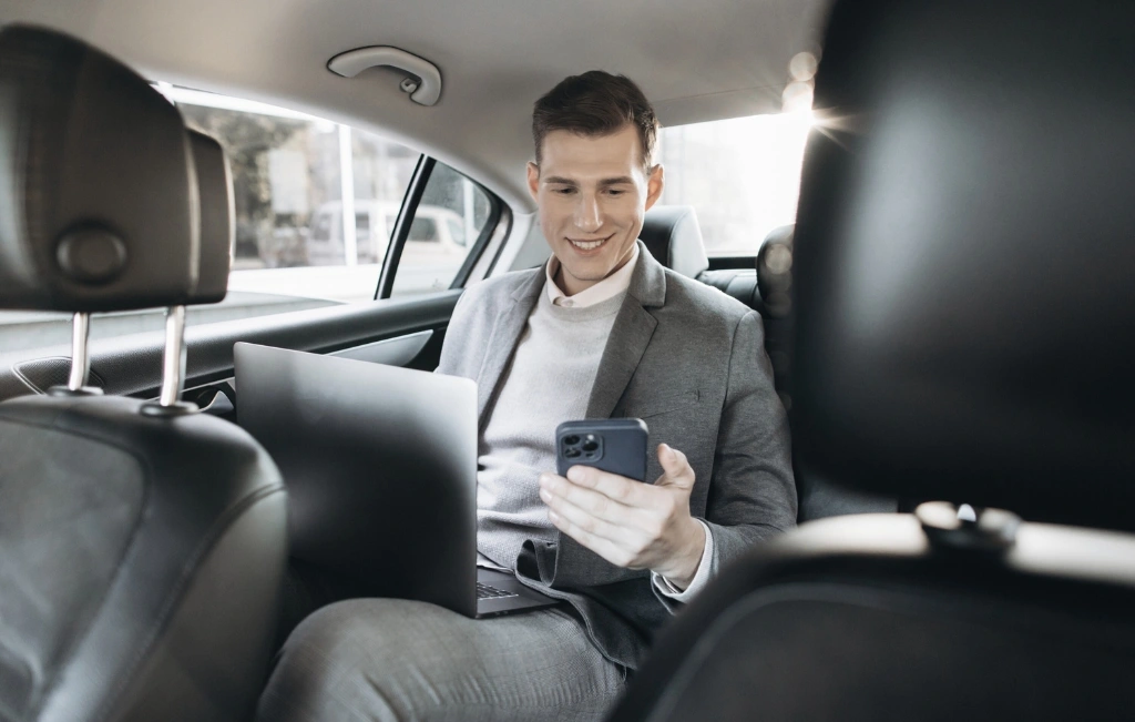 businessman with his phone and laptop inside a hired airport car service