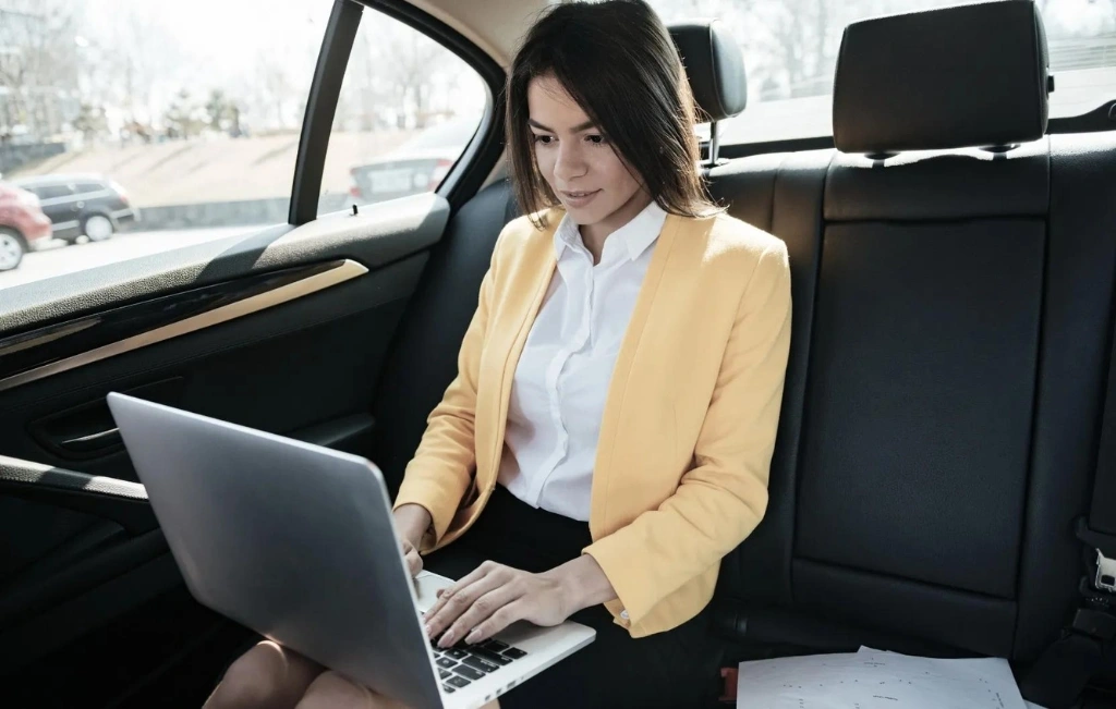 Businesswoman sitting on back seat of car and working during Airport Car Service