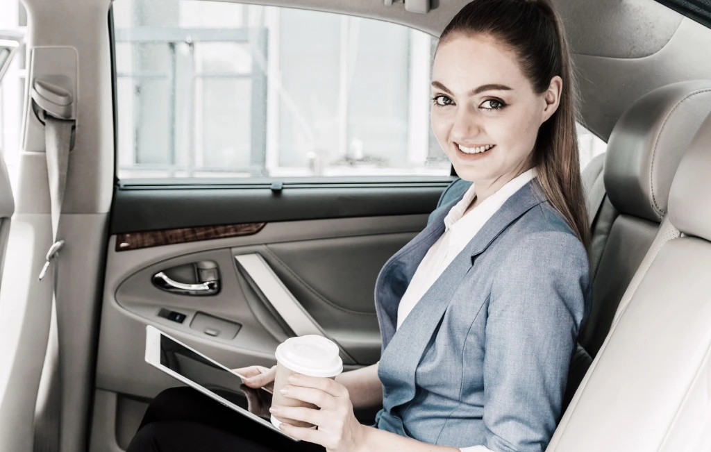 Portrait-of-smiling-businesswoman-holding-disposable-cup-sitting-in-airport-car-service